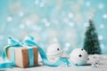 Christmas gift box, jingle bell and blurred fir tree against blue bokeh background. Holiday greeting card.