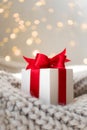 Christmas gift box with red bow on warm knitted sweater and defocused lights Royalty Free Stock Photo