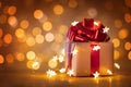 Christmas gift box with red ribbon and lights against golden bokeh background. Holiday greeting card Royalty Free Stock Photo