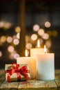 Christmas gift box with three white candles and lights background Royalty Free Stock Photo