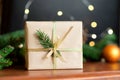 Christmas gift box with Christmas tree branch decor and gold ribbon on a wooden brown background.