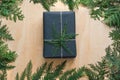 Christmas gift box wrapped in black paper with decor of branch cypress on wooden.