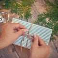 Christmas gift in hands, pine cones, thuja branches on wooden background. Flat lay, top view, copy space