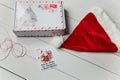 Christmas gift and Santa hat on white wooden table. Inscription on the card: Happiness is snow, sweets and warm mittens.