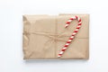 Christmas gift wrapped in craft paper, tied with scourge, decorated with cane candy on white background. Simple minimal style.