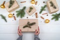Christmas gift wrapping background, copy space. Female hands holding christmas present box wrapped in kraft, top view. Royalty Free Stock Photo