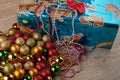 Christmas gifts. Blue glossy box with red bow-knot, decoration balls and beads laying on wooden table Royalty Free Stock Photo