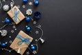 Christmas gifts with blue ribbon, blue balls, fir tree branches, cones, confetti on dark black background with copy space. Flat