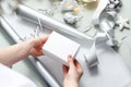 Christmas gifts. A woman wraps a present under a Christmas tree in silver paper.