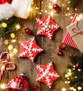 Christmas gingerbread stars, fir branches, red decorations, lights garland, Santa hat, orange and gift boxes on wooden background Royalty Free Stock Photo