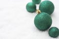 Christmas glitered green baubles, balls isolated on snow. Winter greeting card with copy space. Royalty Free Stock Photo