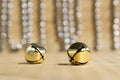 Christmas golden jingle bells on shiny background reflections, silver xmas chain, wooden table