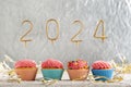 Christmas greeting card with cupcakes and gold sparklers numbers 2024. Holiday muffins with pink buttercream frosting