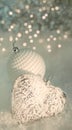 Christmas greeting card. Glass heart and a white ball with pearls on a snow. Blurred gray backdrop of yellow bokeh and light Royalty Free Stock Photo