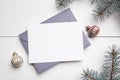 Christmas greeting card mockup with envelope, green fir tree branches and balls on white wooden background, top view, flat lay. Royalty Free Stock Photo