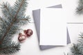 Christmas greeting card mockup with envelope, green fir tree branches and balls on white wooden background, top view, flat lay. Royalty Free Stock Photo