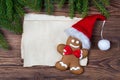 Christmas greeting card, old blank paper sheet, gingerbread man in Santa hat and fir on wooden background