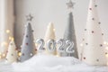 Christmas greeting card with silver number 2022. Yarn wrapped xmas cone trees and garland on background