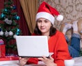 Christmas greetings on the Internet, education, online shopping. Girl in a Santa Claus cap with a laptop at home Royalty Free Stock Photo