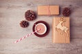 Christmas handmade gift boxes with cup of chocolate and pine corn on wooden table. View from above