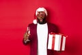 Christmas. Handsome african american man in party glasses and santa hat, holding new year gift and glass of champagne Royalty Free Stock Photo