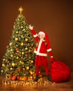 Christmas Happy Child in Elf Costume Holding Red Santa Bag with New Year Gifts under Xmas tree. Decorate Illuminated Home Room