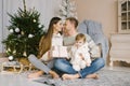 Christmas happy family. Portrait of a father, mother and daughter sitting at home near the Christmas tree. Parents kiss