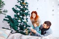 Christmas happy family of three persons decorating fir tree with gift boxes over white bedroom background Royalty Free Stock Photo