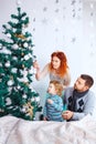 Christmas happy family of three persons decorating fir tree with gift boxes over white bedroom background Royalty Free Stock Photo