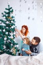 Christmas happy family of three persons decorating fir tree with gift boxes over white bedroom background Royalty Free Stock Photo