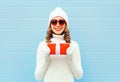 Christmas happy smiling young woman with gift box wearing a knitted hat sweater sunglasses over blue Royalty Free Stock Photo