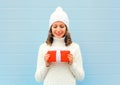 Christmas happy smiling young woman holds gift box in hands wearing a knitted hat sweater over blue Royalty Free Stock Photo