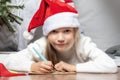 Christmas helper child writing letter to Santa Claus in red hat. smiling girl making wish list or letter to santa at Royalty Free Stock Photo