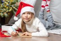 Christmas helper child writing letter to Santa Claus in red hat. smiling girl making wish list or letter to santa at Royalty Free Stock Photo