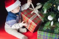 Christmas holiday. Baby in Santa hat opening box of gifts
