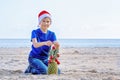 Christmas holiday. Boy in red Santa hat decorating pineapple as a Christmas tree on a sunny sandy beach by the sea