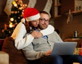 Christmas holiday. Female in Santa`s hat hugging a man using a laptop. Royalty Free Stock Photo