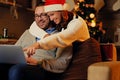 Christmas holiday. Female in Santa`s hat hugging a man using a laptop. Royalty Free Stock Photo