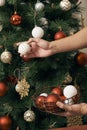 Christmas holiday green and red decoration. Guy`s hands ornamenting the pine tree with a white ball decoration Royalty Free Stock Photo