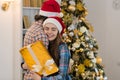 Christmas Holiday Happy Couple Wear New Year Santa Hat Cap, Man And Woman Embracing Near Decorated Tree Holding Present Royalty Free Stock Photo