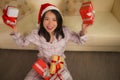 Christmas holiday lifestyle portrait at home of young beautiful and happy Asian Chinese woman in pajamas and Santa hat  holding Royalty Free Stock Photo