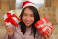 Christmas holiday lifestyle portrait at home of young beautiful and happy Asian Chinese woman in pajamas and Santa hat  holding Royalty Free Stock Photo