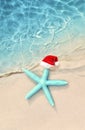 Christmas holidays concept. Top view of starfish in santa claus hat on summer sand beach Royalty Free Stock Photo