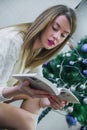 christmas, holidays and people concept - happy young woman reading book at home. Happy beautiful woman with make-up Royalty Free Stock Photo