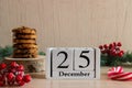 Christmas home concept. Wooden calendar dated December 25, chocolate cookies on wooden stand, red berries, and Christmas tree