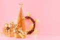 Christmas home decor in golden color - Christmas tree, glowing garland, wreath, decorations, present on soft light pink background Royalty Free Stock Photo
