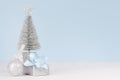 Christmas home decoration - silver fir with festive gift box with blue silk bow and sparkles ball on white wood board and pastel.