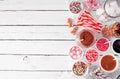 Christmas hot cocoa bar with assorted sweet toppings. Side border on a white wood background.