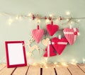Christmas image of fabric red hearts and blank frame, garland lights, hanging on rope in front of blue wooden background Royalty Free Stock Photo