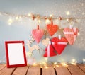 Christmas image of fabric red hearts and blank frame, garland lights, hanging on rope in front of blue wooden background Royalty Free Stock Photo